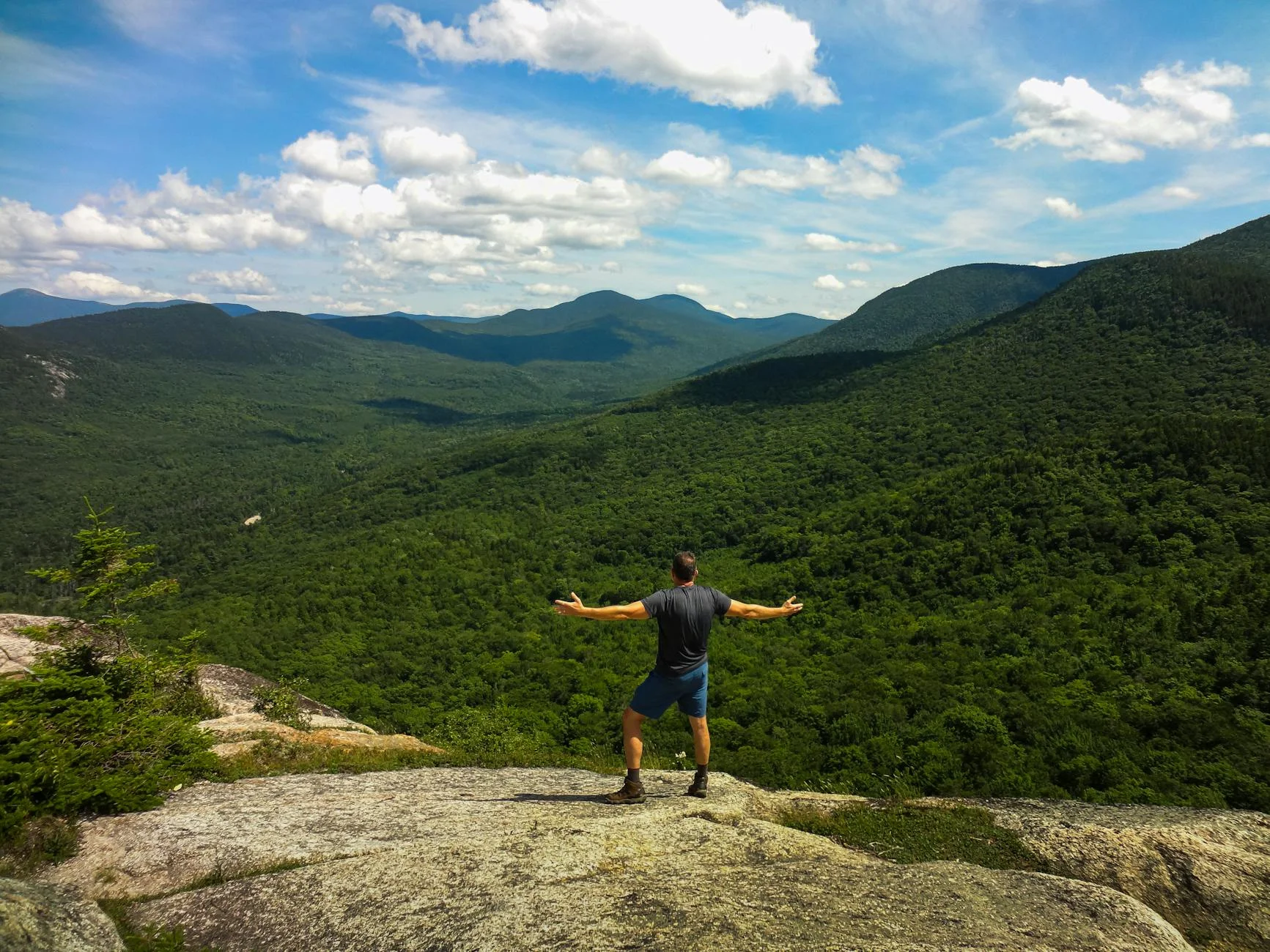 Hiker on rocky summit overlooking lush valleys