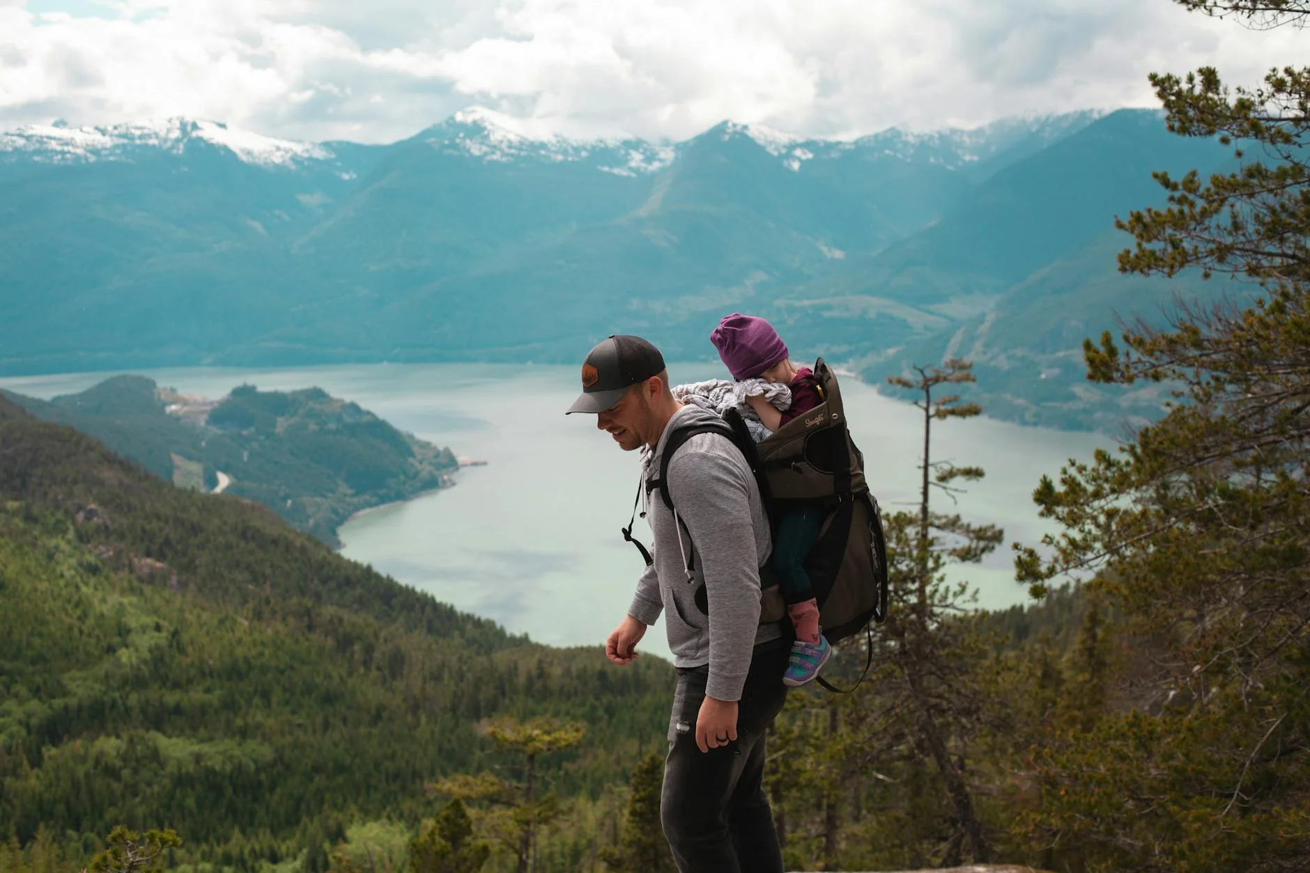 Father carrying child on a mountain hike with lake views