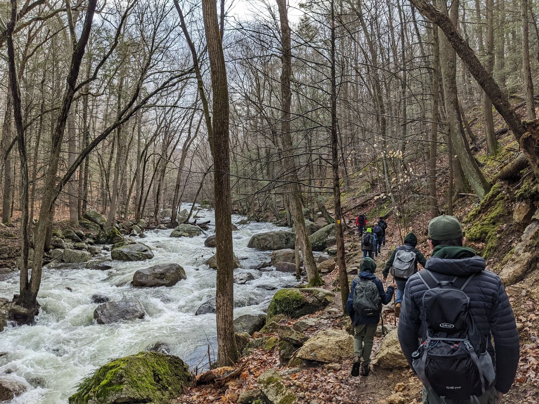 Hikers on a rocky trail beside a fast-flowing stream