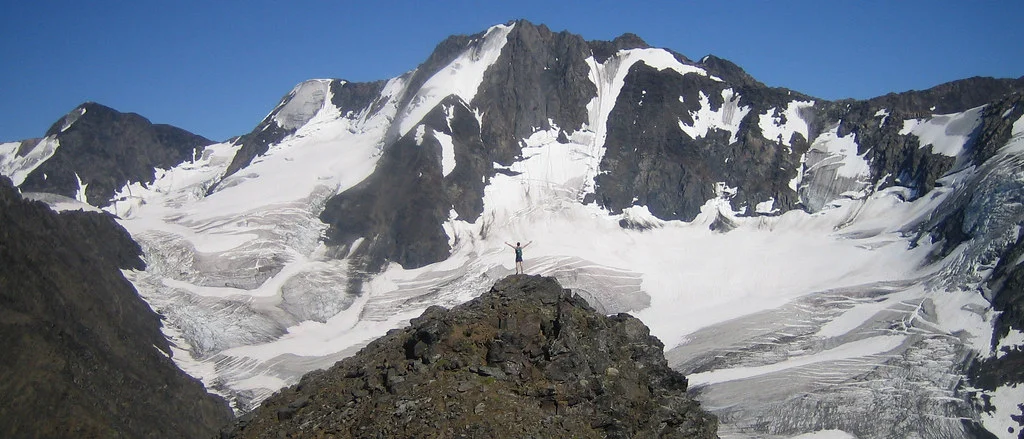 Hiker on a bare summit ridge with mountain panorama